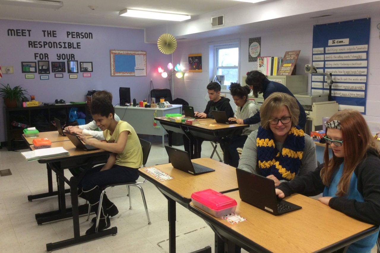 Students working on laptops with teachers in a Spectrum classroom